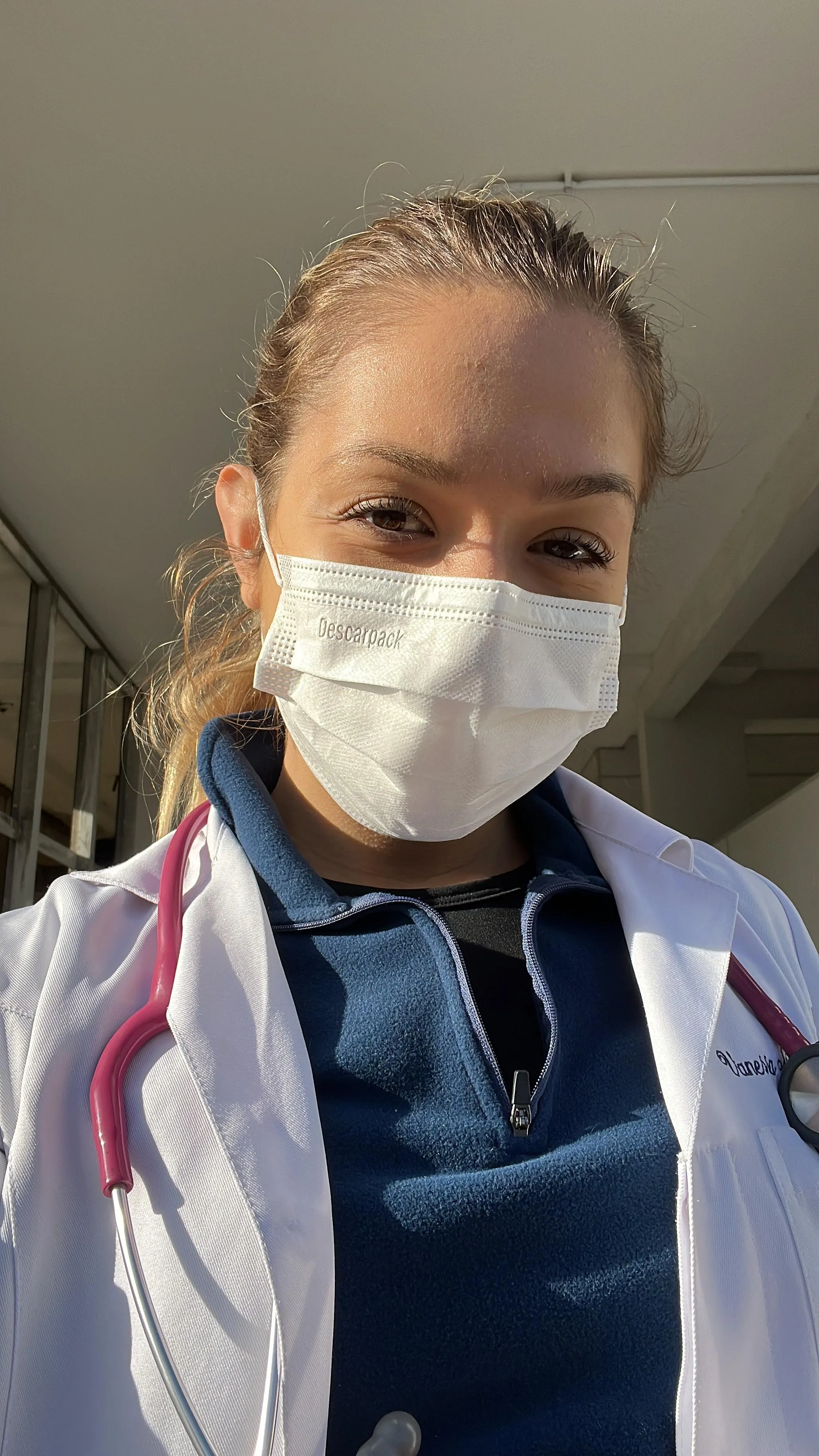 Vanessa de máscara cirúrgica e jaleco, em plantão na UPA